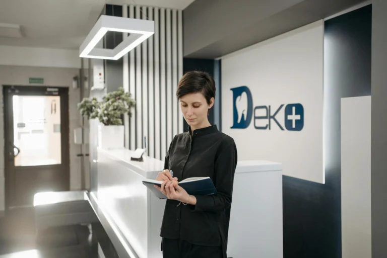 Female receptionist writing notes at dental office reception. Professional healthcare setting.