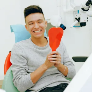 Smiling man holding a mirror during a dental checkup in a clinic setting.