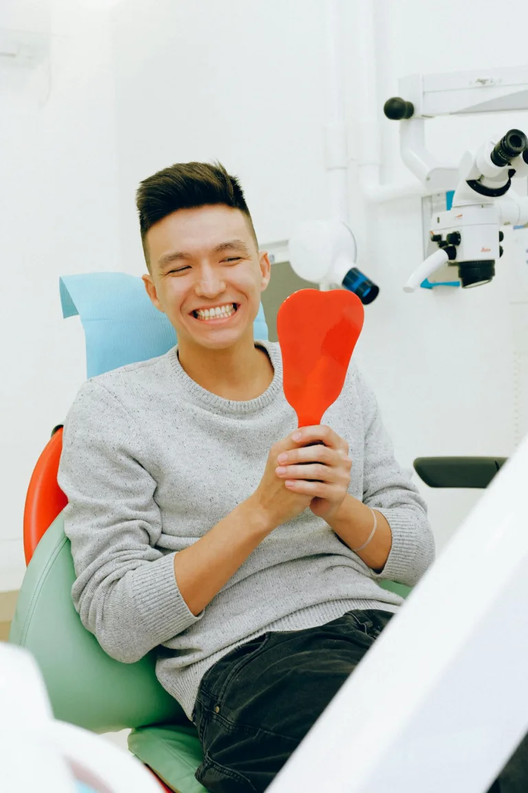 Smiling man holding a mirror during a dental checkup in a clinic setting.